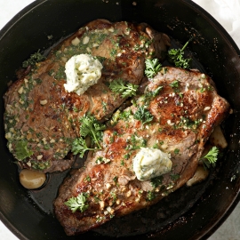 two steaks in a skillet topped with butter
