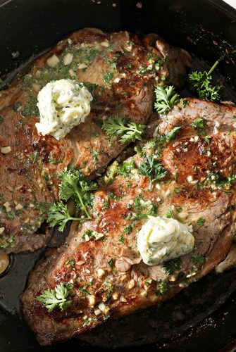 two steaks in a skillet topped with butter