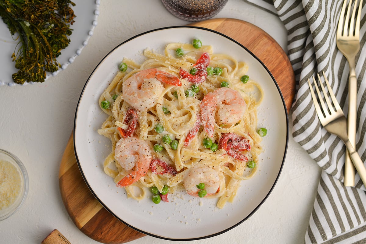 overhead of shrimp alfredo on a white serving plate with a side of broccolini 