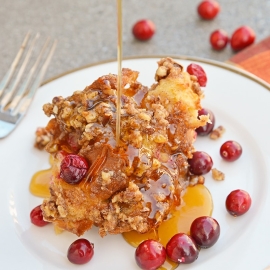 maple syrup pouring cranberry french toast casserole on a white serving plate