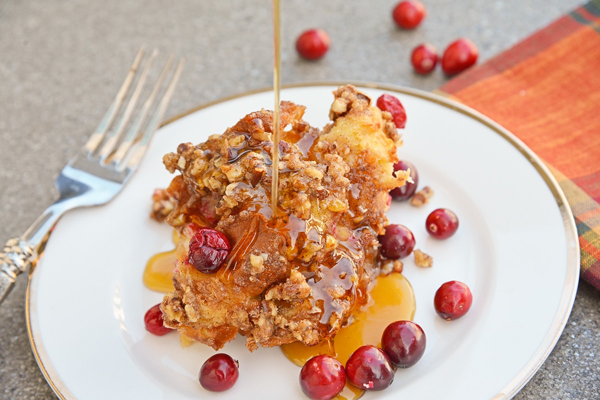 maple syrup pouring cranberry french toast casserole on a white serving plate