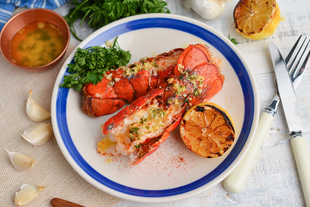 two grilled lobster tails on a white plate with garlic sauce and lemon