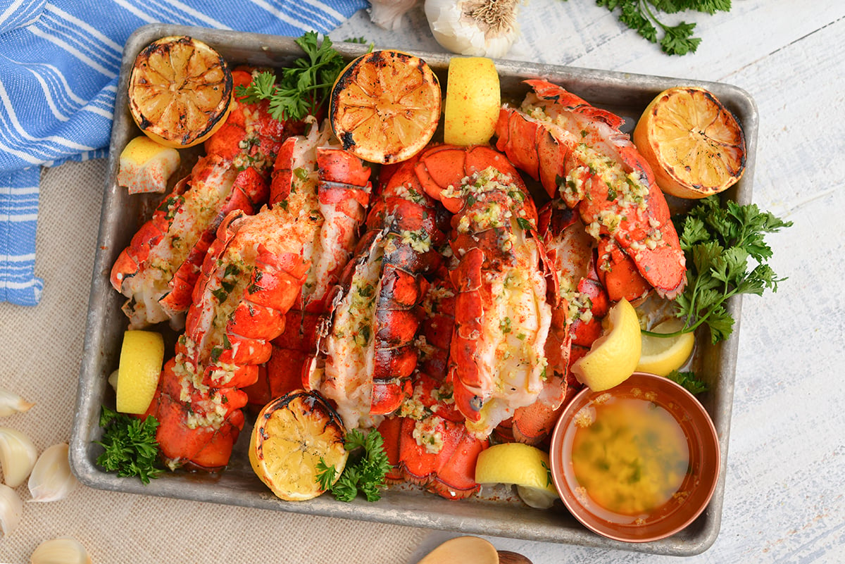overhead tray of grilled lobster tails with lemons and garlic butter sauce