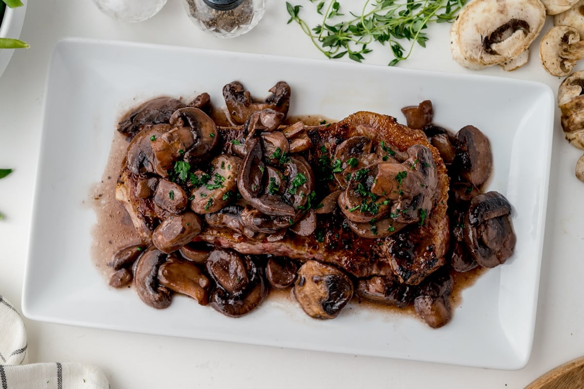 mushrooms over a NY strip steak on a white serving platter