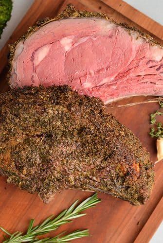 overhead of rare rib roast on a cutting board with fresh herbs and garlic cloves