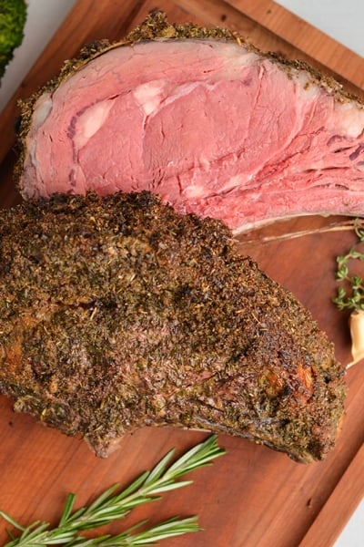 overhead of rare rib roast on a cutting board with fresh herbs and garlic cloves