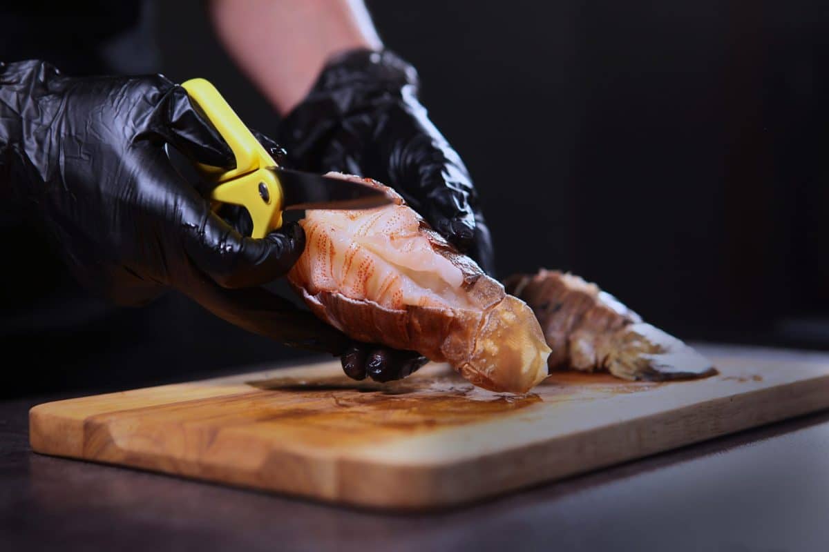 hands butterflying a lobster tail using kitchen shears 