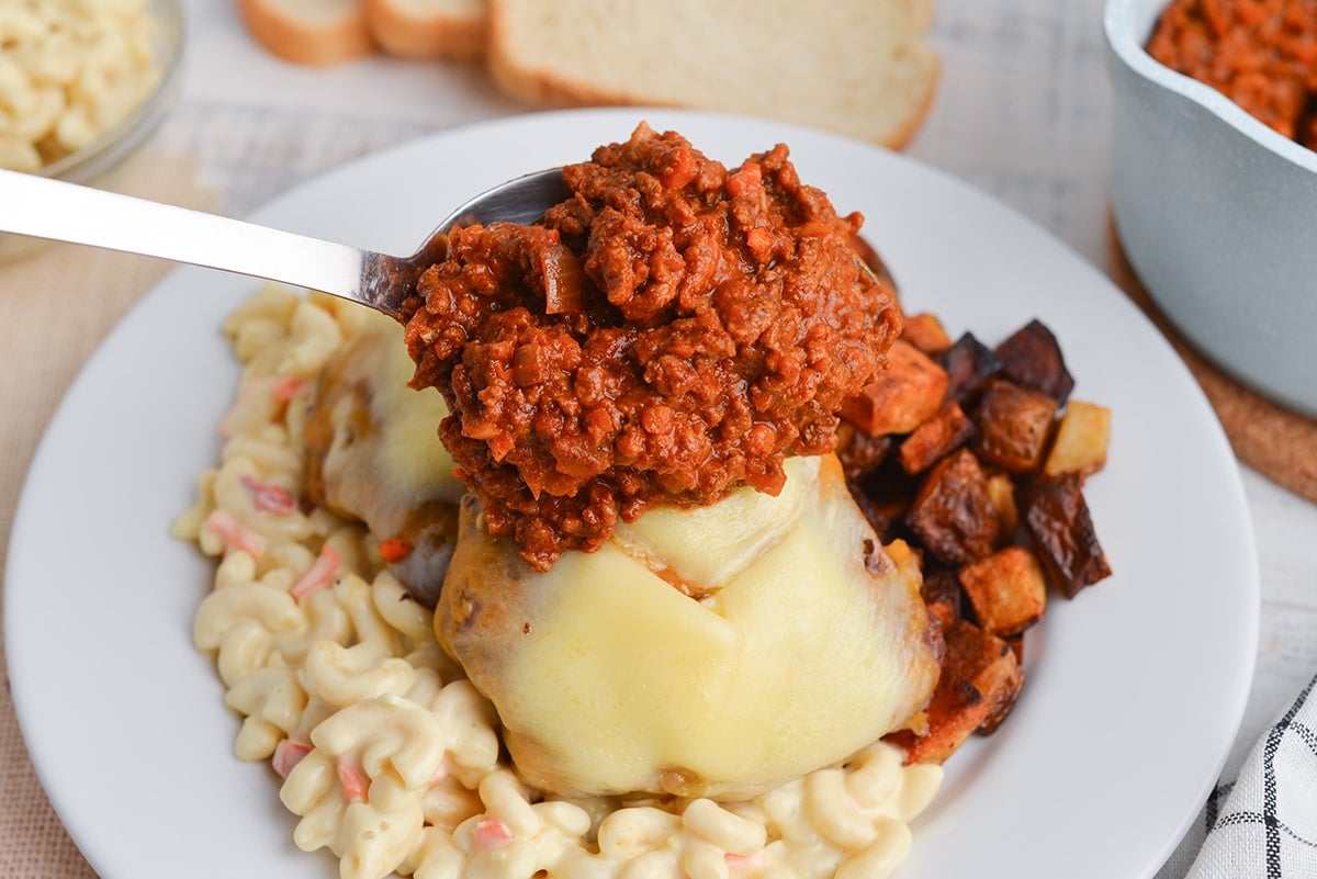 spooning meat sauce over a garbage plate