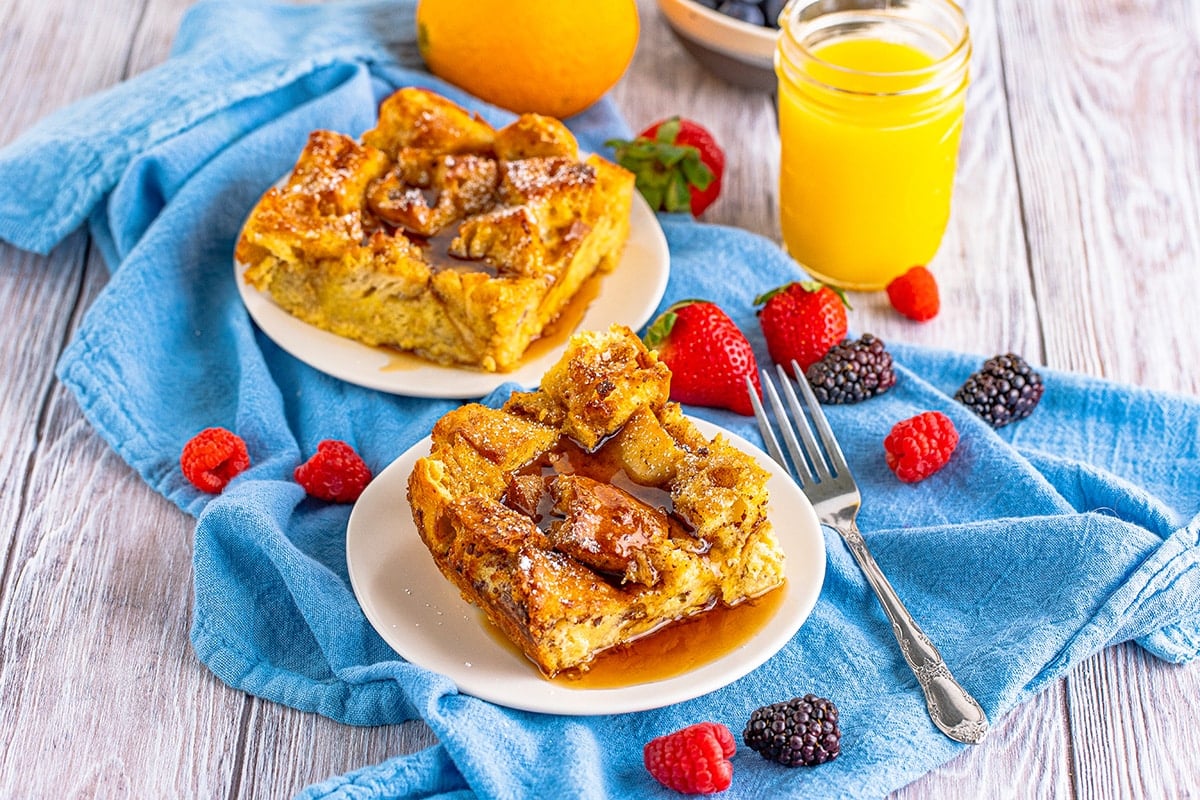 two slice of overnight french toast bake on plates with fresh berries and orange juice