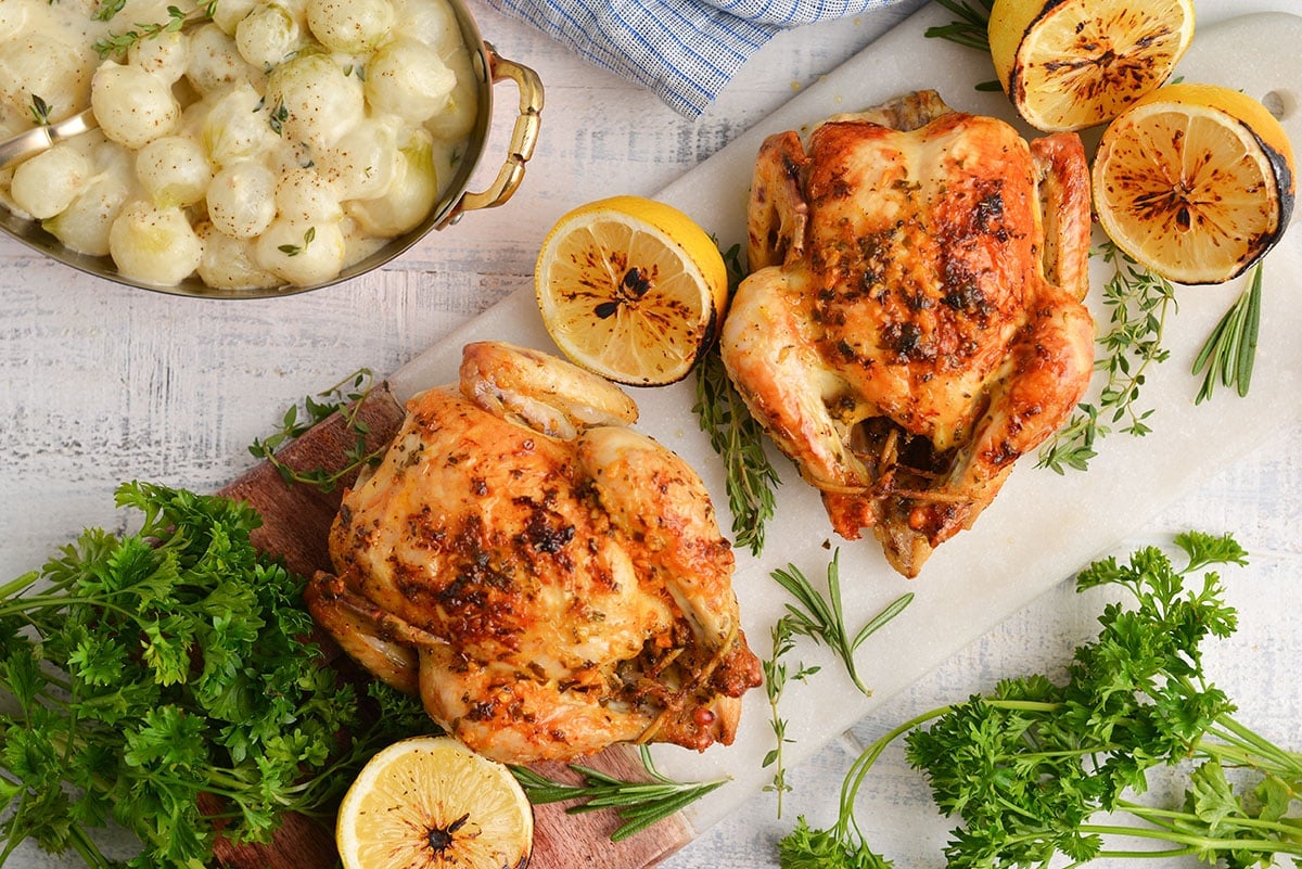 overhead of two cornish hens on a serving platter with lemon wedges