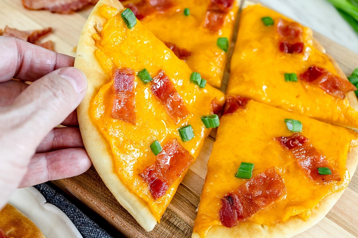 hand holding slice of bacon cheddar flatbread