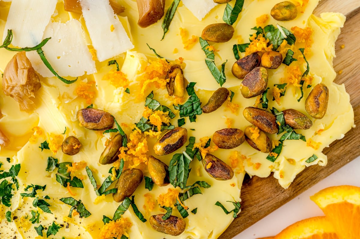 close up of pistachios, orange and mint on a butter board