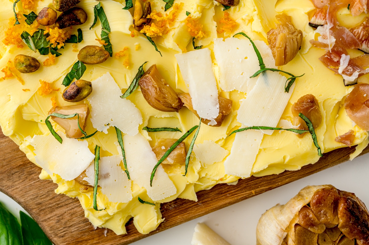 close up of parmesan cheese shaves and roasted garlic on a butter board