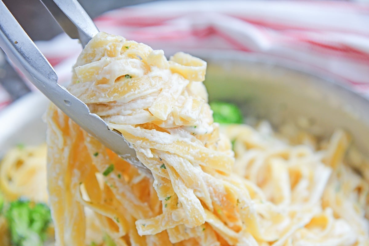 tongs holding pasta with alfredo sauce