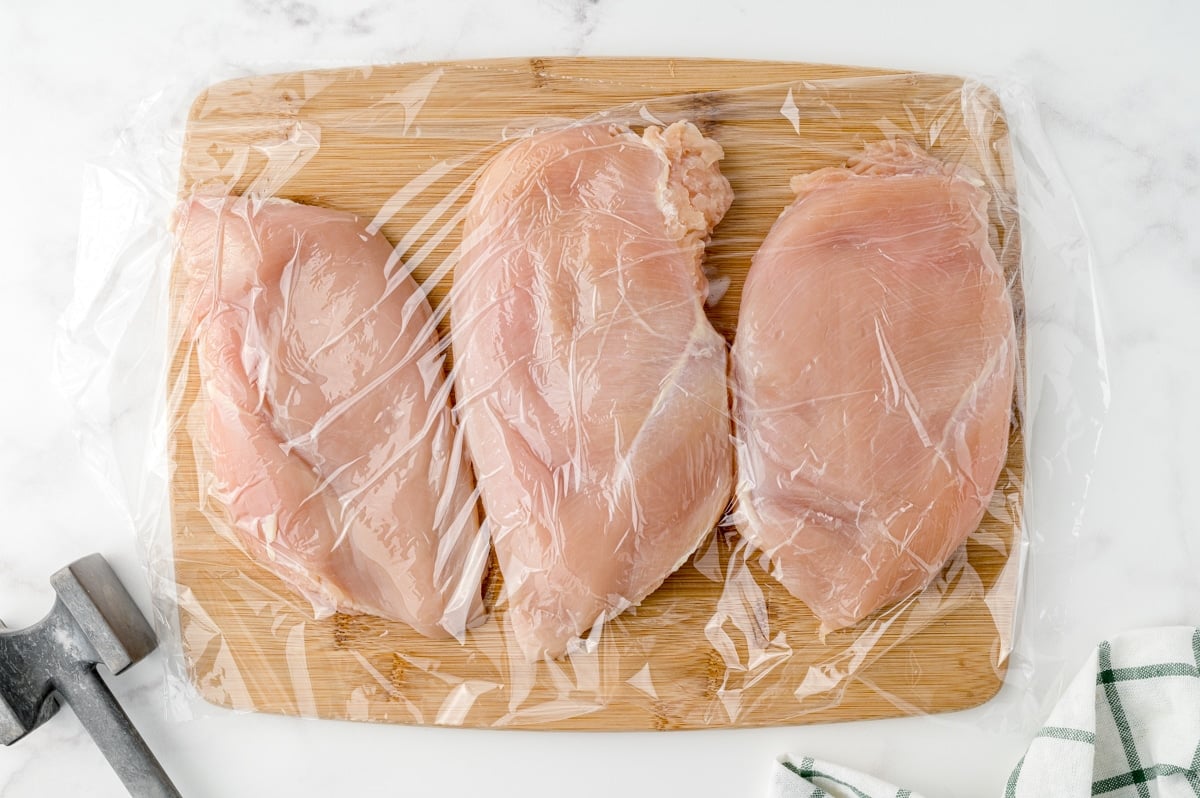chicken breasts on a cutting board covered in plastic wrap