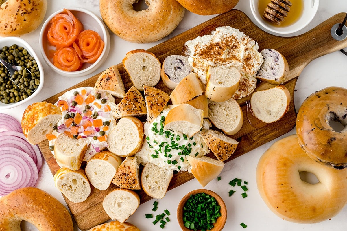 overhead shot of bagels dipping into cream cheese board
