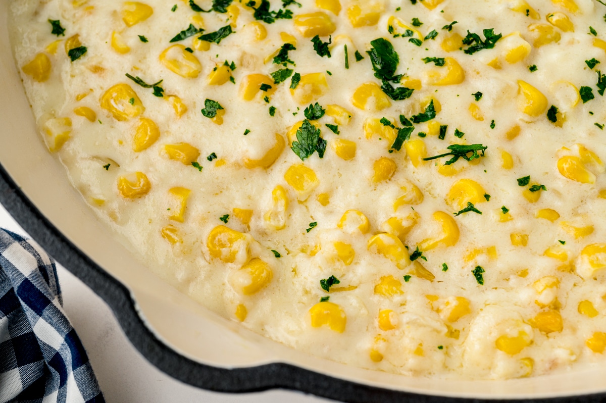 close up of creamed corn in a white skillet with parsley