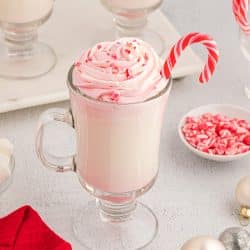 angle of white hot chocolate in a glass with ppermint whipped cream and candy canes