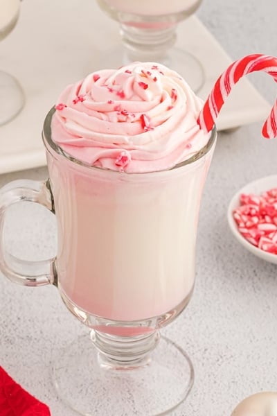 angle of white hot chocolate in a glass with peppermint whipped cream and candy canes