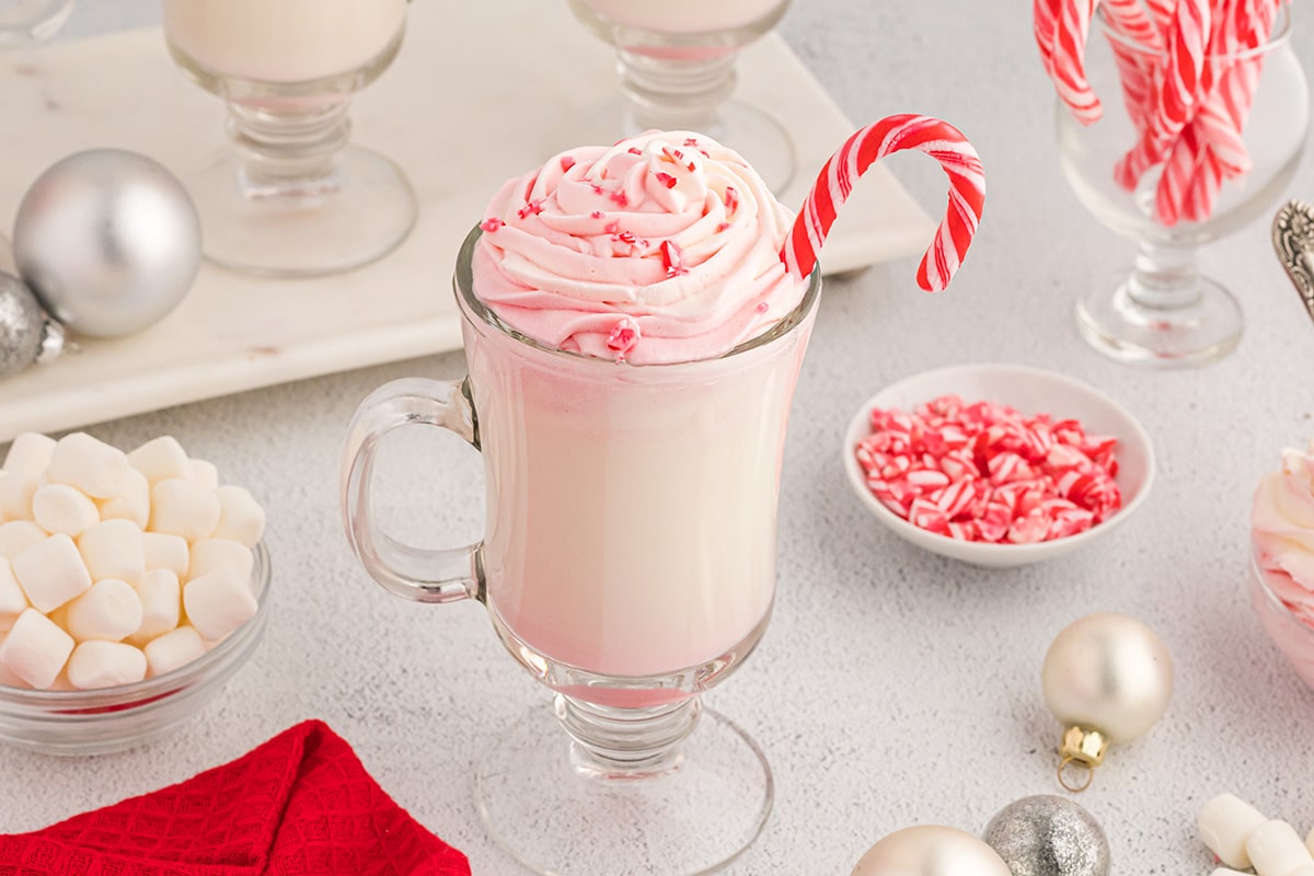 angle of white hot chocolate in a glass with ppermint whipped cream and candy canes
