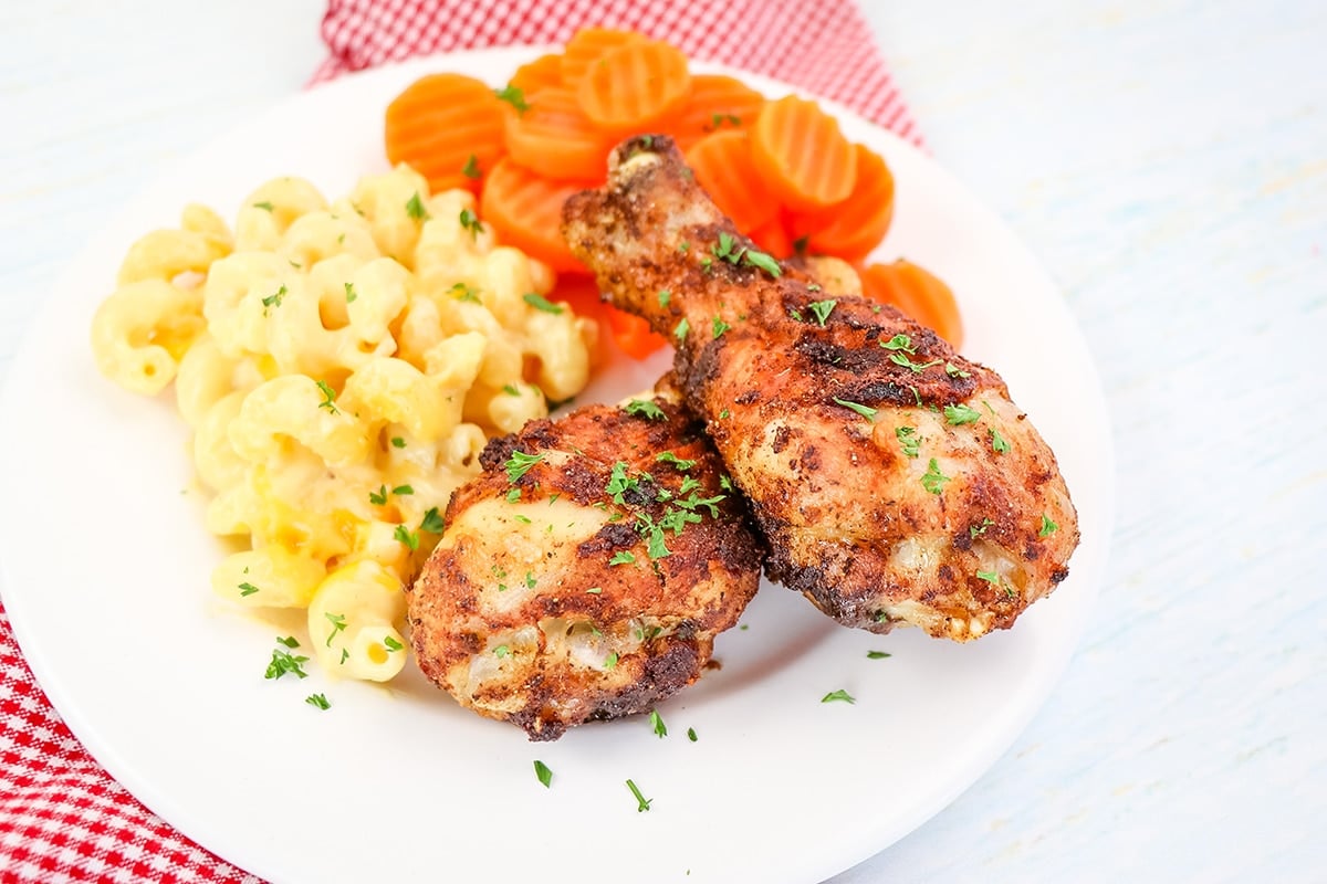 two drumsticks on plate with carrots and mac and cheese
