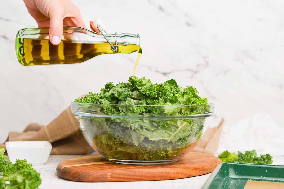 olive oil pouring over a bowl of kale