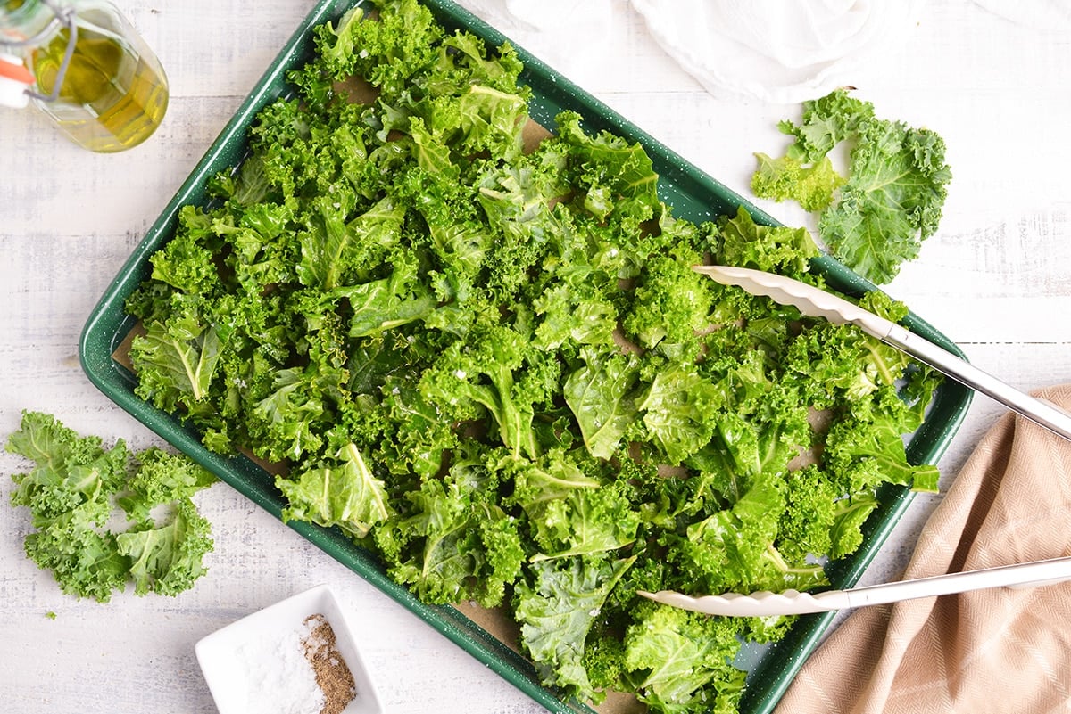 raw kale on a baking sheet with tongs