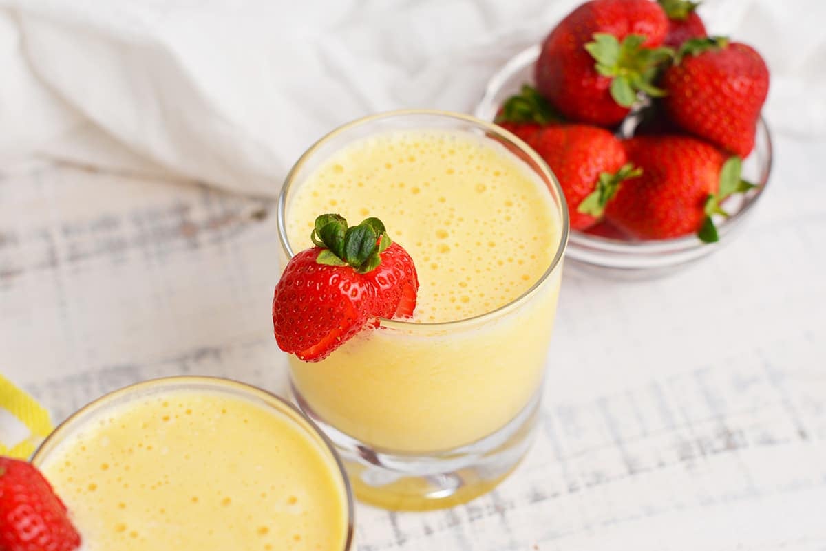 frothy mango smoothie with bowl of strawberries