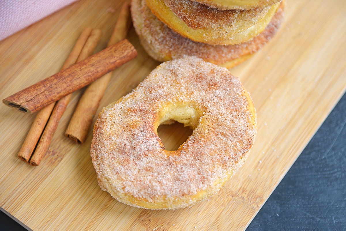 cinnamon sugar donuts on a wood cutting board with cinnamon sticks