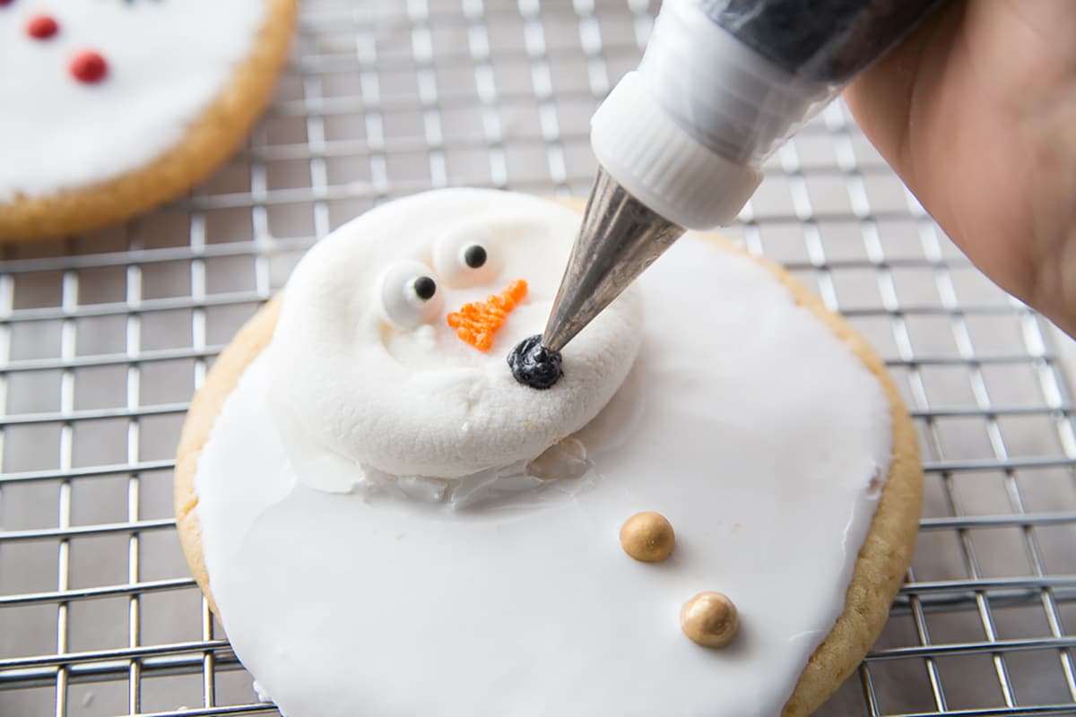 piping mouth onto snowman cookie