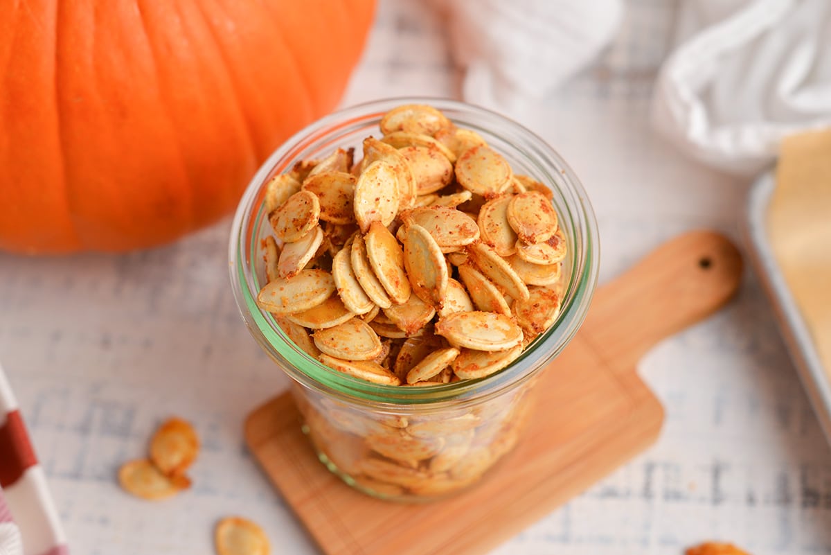 angle view of pumpkin seeds in a glass jar with a pumpkin
