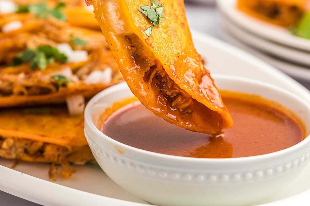 dipping chicken taco in a bowl of birria sauce