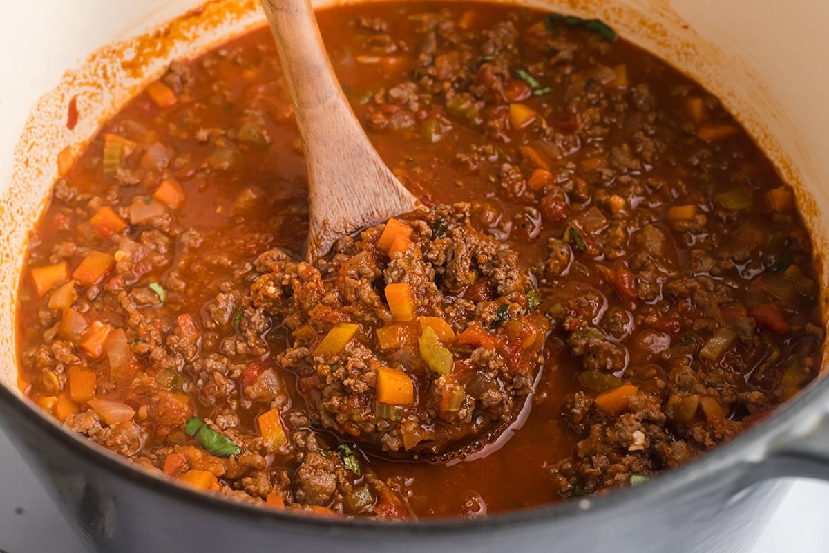 wooden spoon stirring bolognese sauce