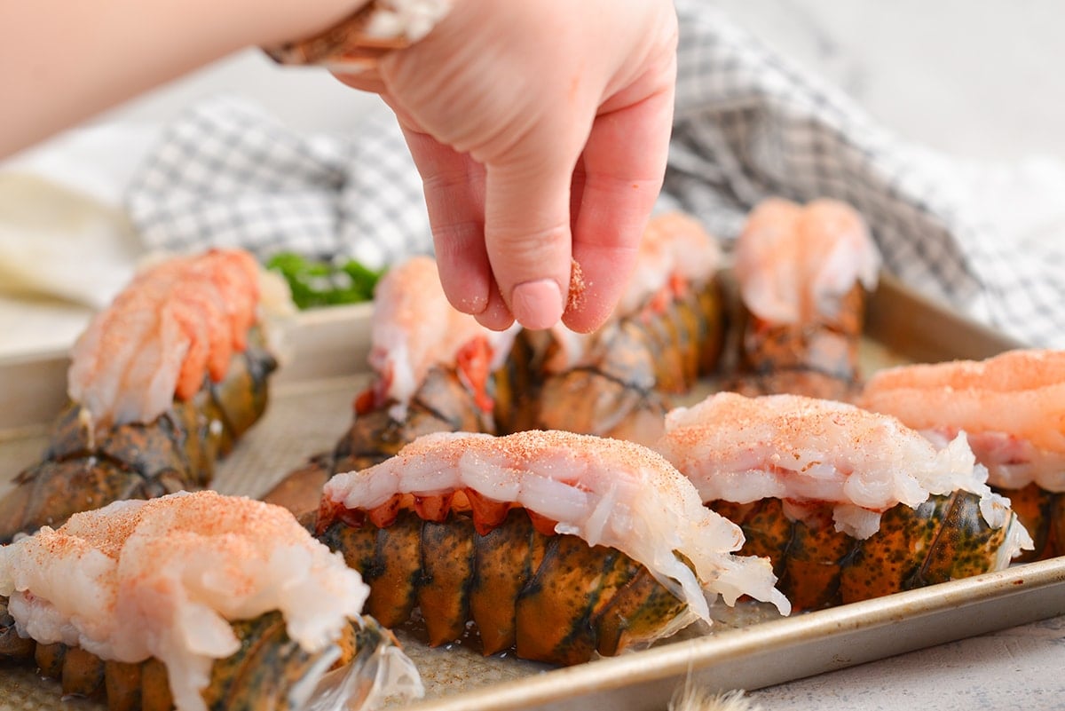 hand sprinkling seasoning on lobster tails