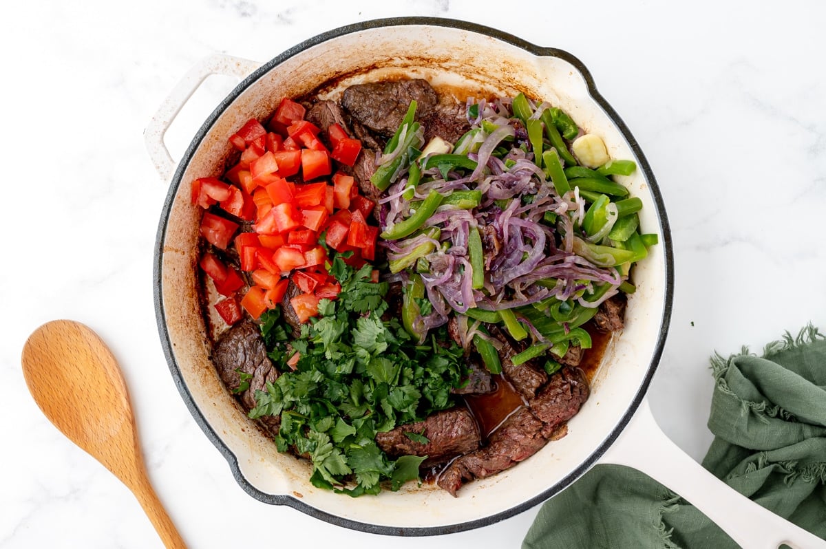 adding tomatoes and cilantro to lomo saltado