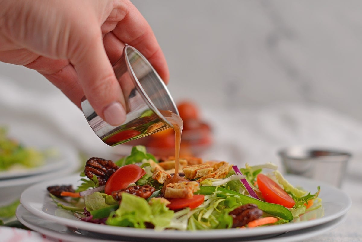 hand pouring dressing over a small salad