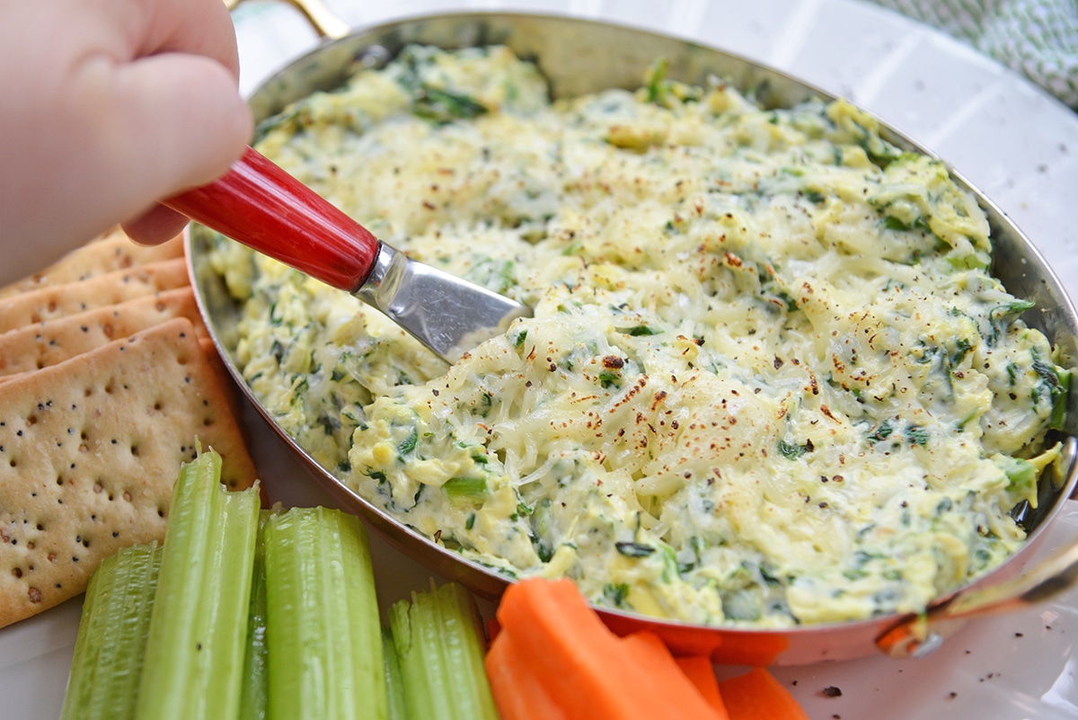 knife digging into spinach and artichoke dip