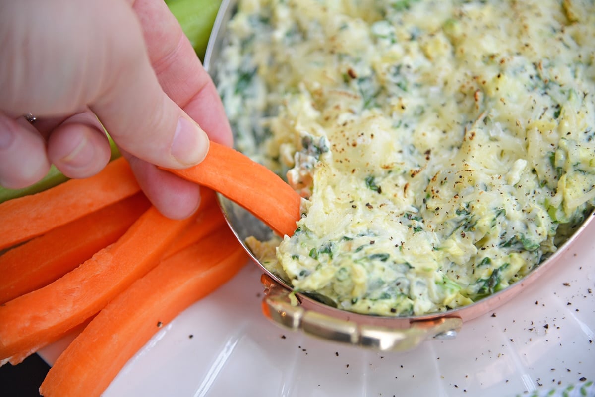 carrot dipping into hot spinach and artichoke dip
