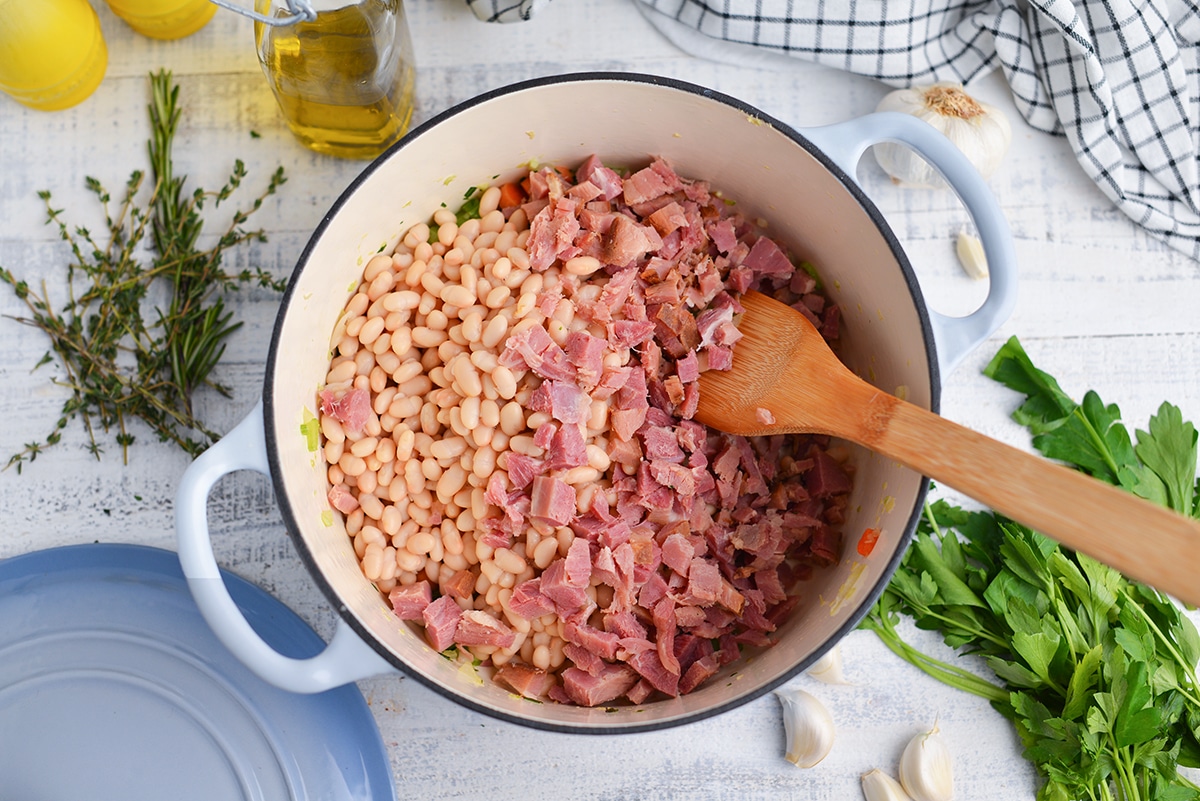 diced ham and white beans in a dutch oven with a wooden spatula