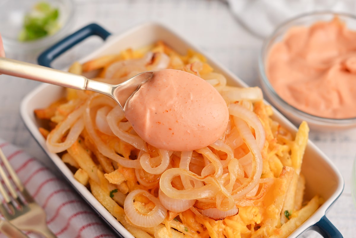 spooning sauce over cheesy fries with onions