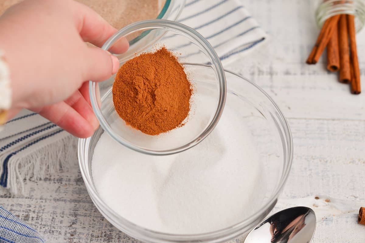 pouring cinnamon into a bowl of white sugar