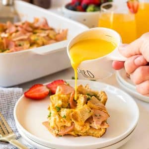 hand pouring hollandaise sauce on slice of breakfast casserole