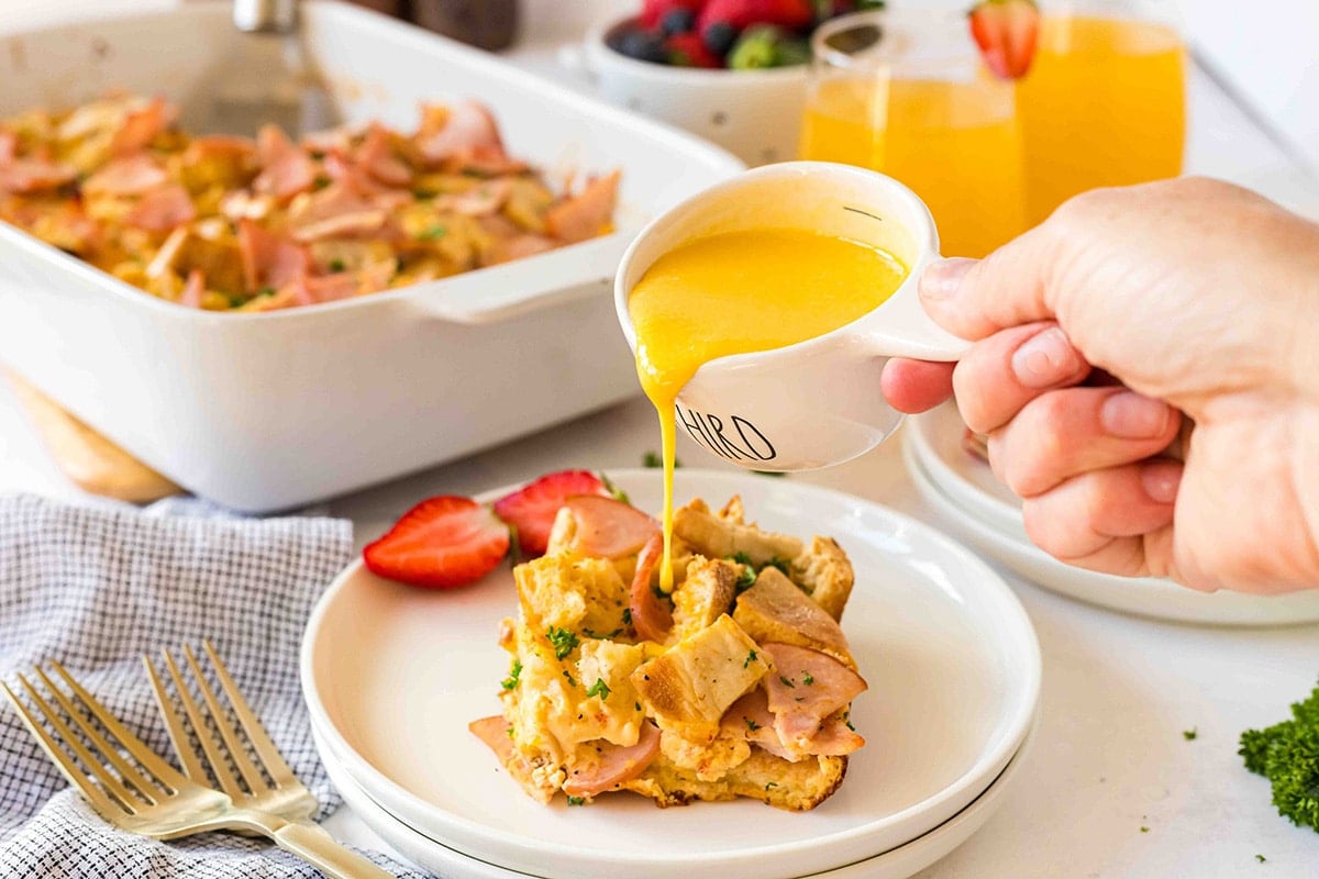 hand pouring hollandaise sauce on slice of breakfast casserole