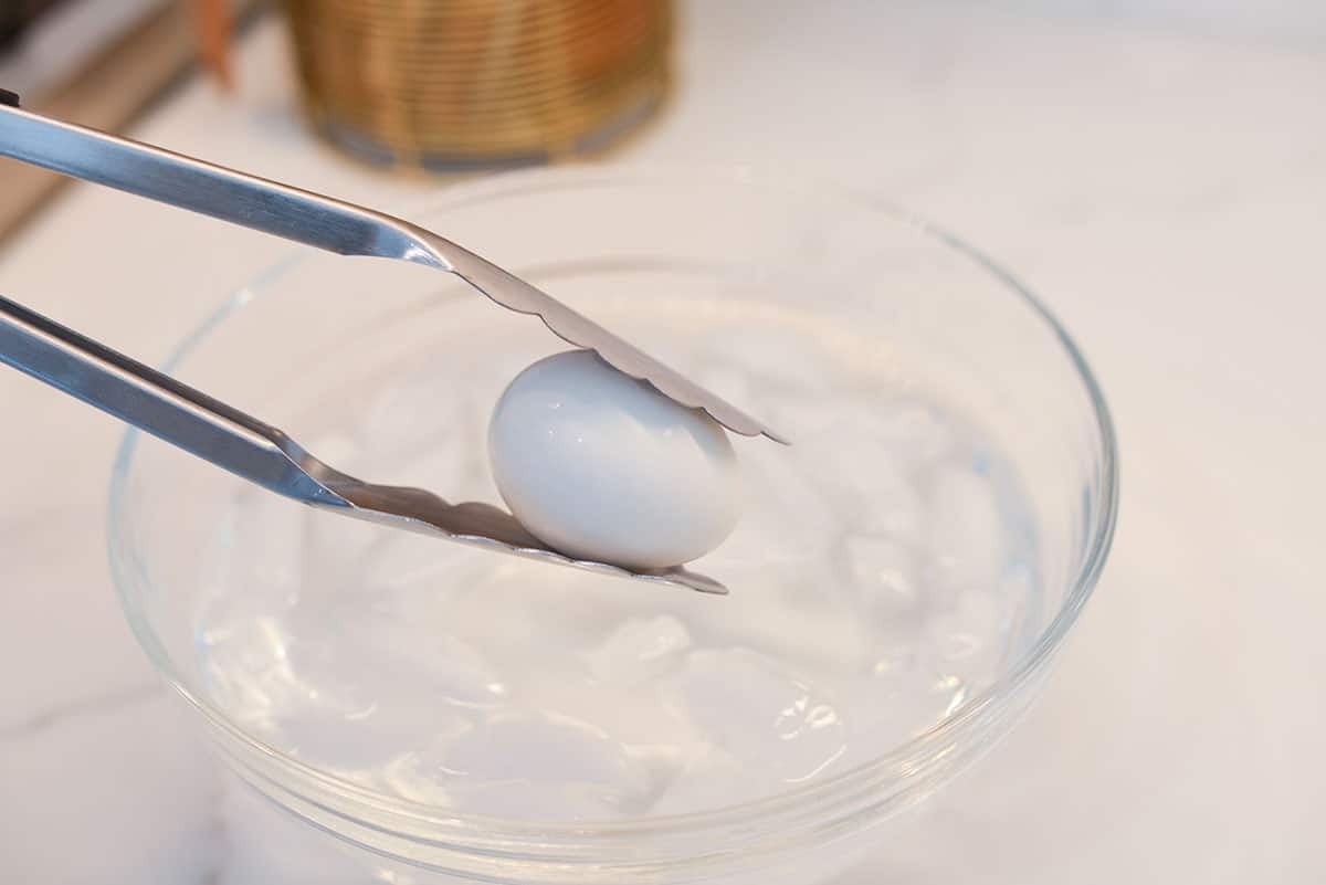 tongs holding an egg going into an ice bath