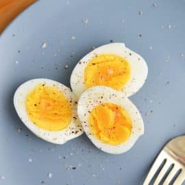 three hard boiled egg halves on a blue plate sprinkled with salt and pepper