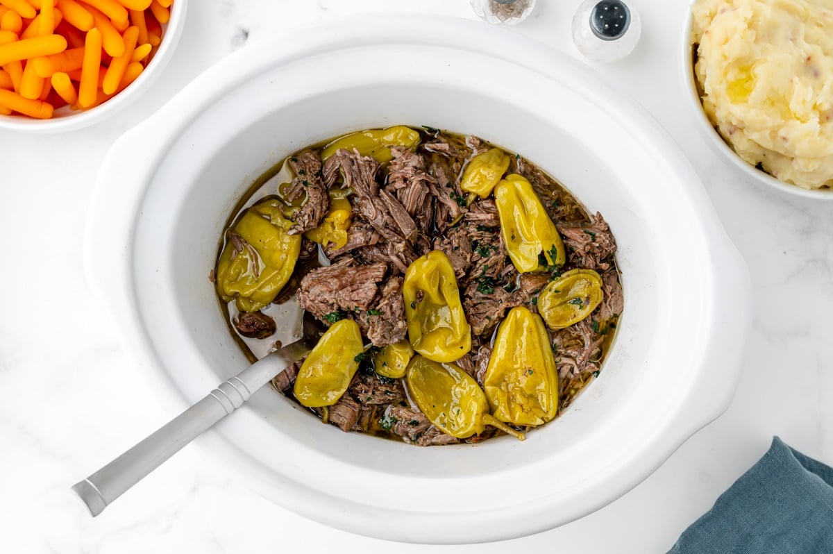 spoon in pepperoncinis in crock pot with shredded beef