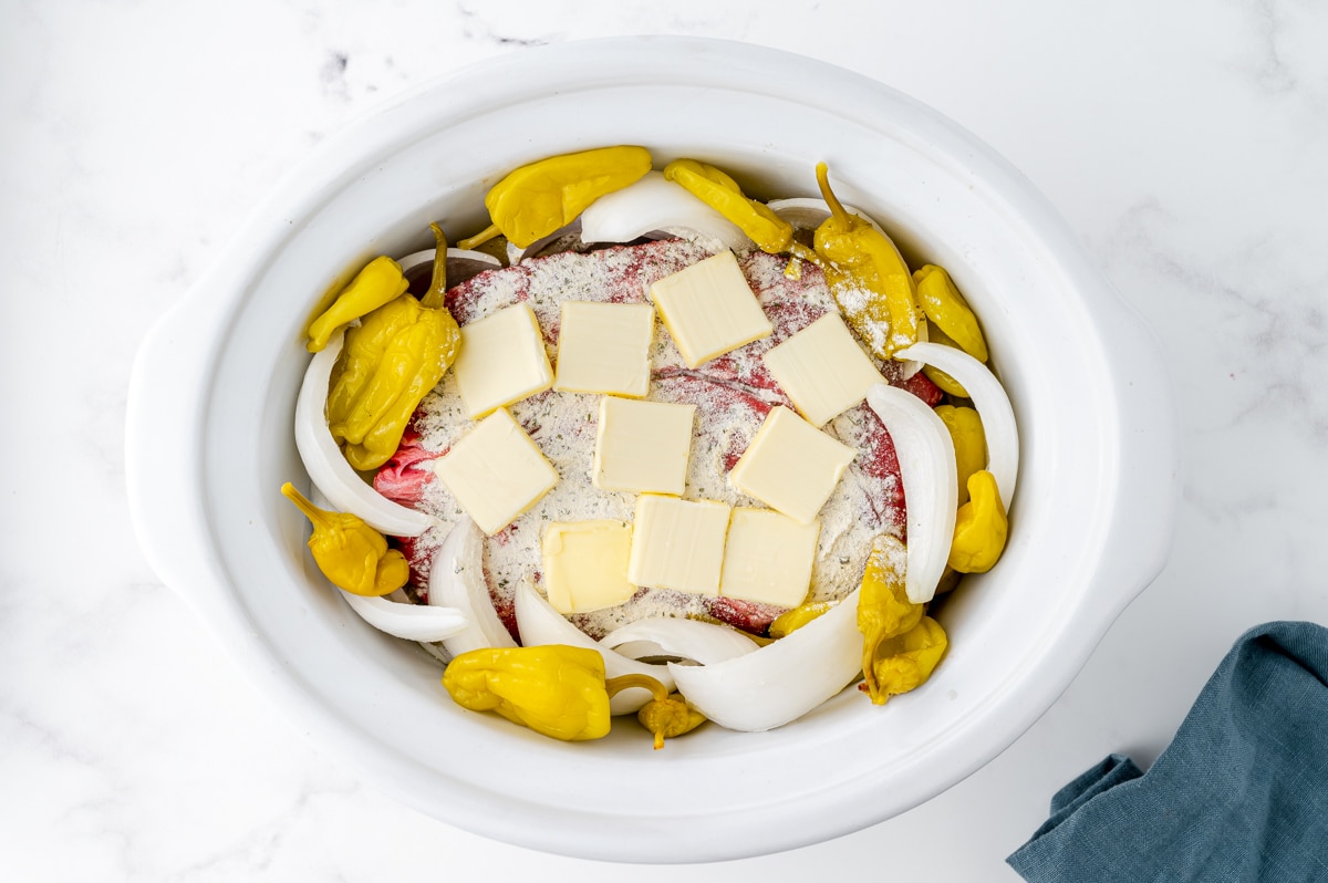 butter and seasoning added to pot roast in crock pot