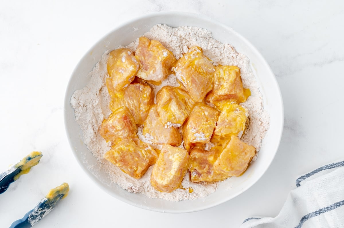 egg coated chicken pieces on bowl of flour