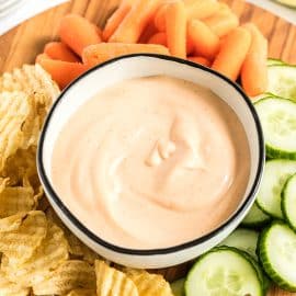 angled shot of sriracha aioli in bowl surrounded by veggies and chips