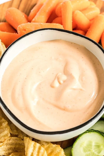 angled shot of sriracha aioli in bowl surrounded by veggies and chips